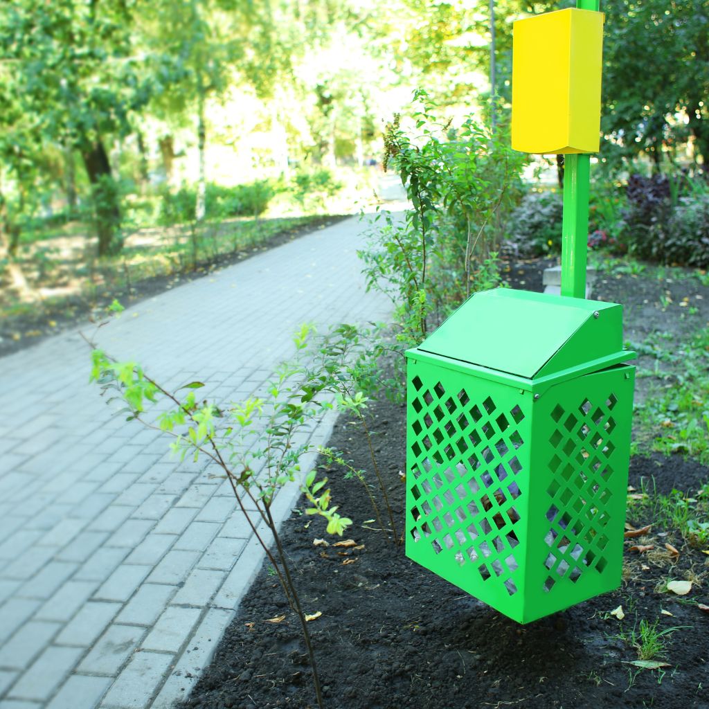 Green decorative trash bin with yellow top on park pathway