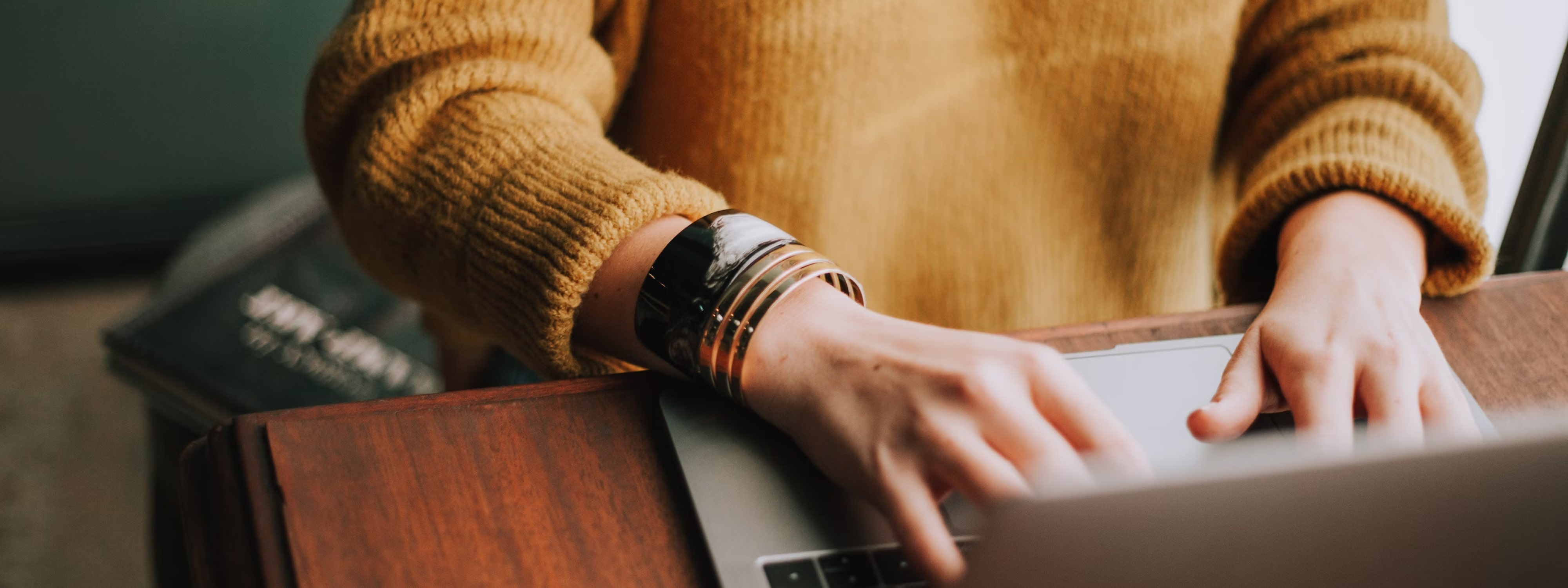 Person in mustard sweater typing on laptop with metal watch